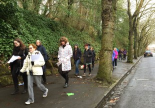 Walking group walk along a pavement surrounded by trees.