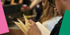 Close up photo of people standing in a room reading books.