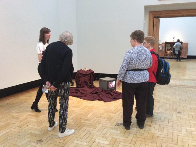 The group looking at Ruth Barker's installation for her performance The Foot Exerts Pressure on the Surface of the Glass. Dress by Lesley Hepburn. (Credit: Alice)