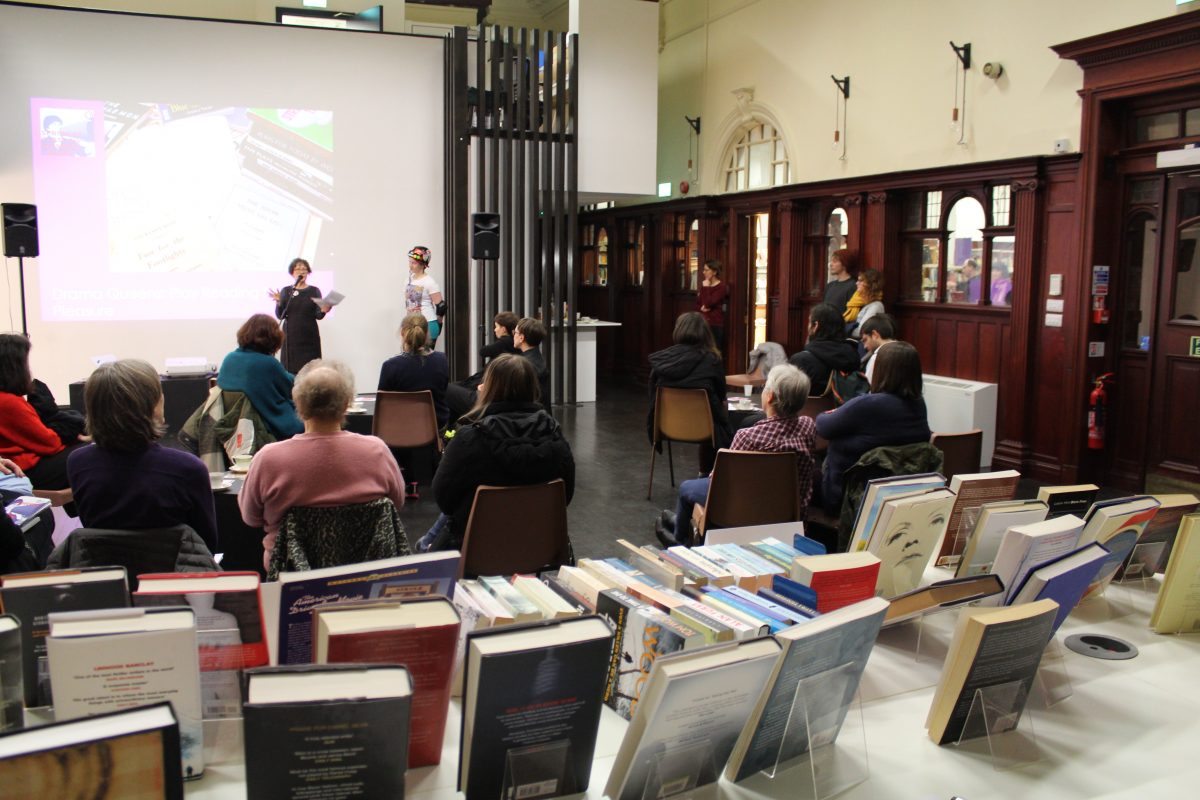 Spring Programme Launch 2017. A woman speaks in front of a group of seated people and here is a book sale taking place in the foreground.