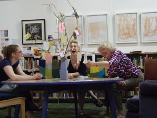 Three volunteers sitting round a table laughing while reading messages on a "sharing tree"