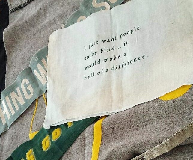 Layered fabric with indistinct text in background. Words on white text in foreground which reads 'I just want people to be kind.. it would make a hell of a difference'.