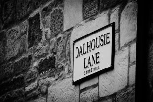 Close up black and white photograph of Dalhousie Lane street sign which is on a stone wall.