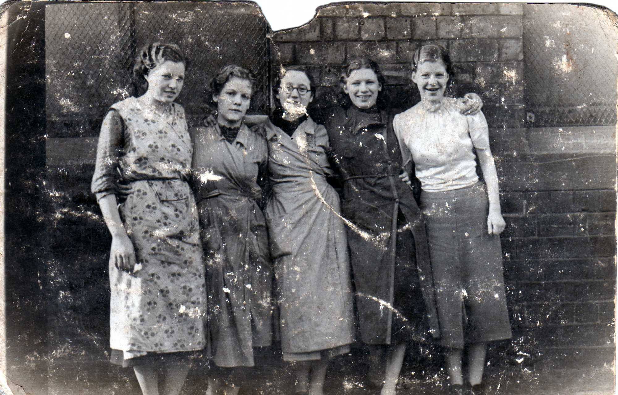 Black and white photo of a group of women standing with their arms around one another outside.