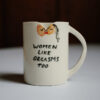 Women Like Orgasms Too Mug. At the top of the mug there are two figures kissing and here there is a small triangle cut out of the rim of the mug.
