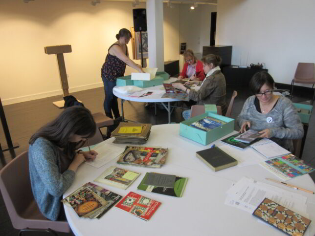 Women gathered round tables with objects on the tables in front of them.