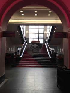 Photo taken from the bottom of the stairs in the National Library of Scotland. They are a wide set of stairs which have a vinyl covering that creates a portrait of Muriel Spark.