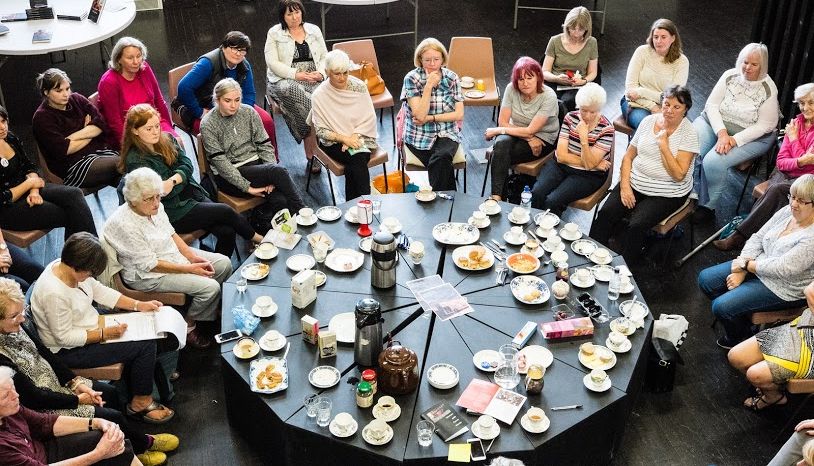 Story Café attendees sit in a circle with cups of tea.