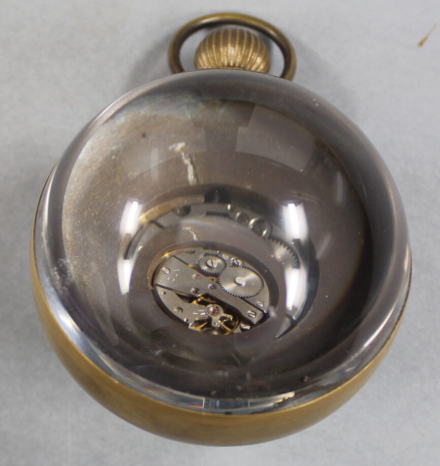 Back of paperweight clock, the clockwork visible through the round glass back