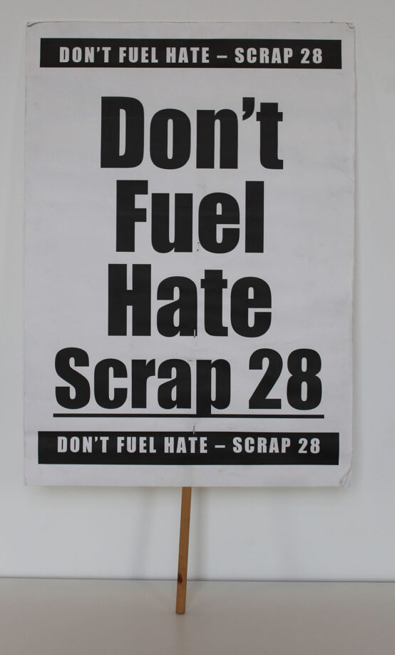 Protest placard reading "Don't Fuel Hate Scrap 28" in bold sans serif text
