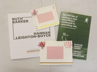 An exhibition catalogue with the names Ruth Barker and Hannah Leighton-Boyce sits on a white table. On top of the catalogue are two postcards and to the right of the image is a green brochure for GWL's spring programme. The two postcards are very similar. In the centre is a rectangle of pink paper. To the top left is a loop of ribbon stuck down. To the top right are small red hearts glued down to the page in a cluster. At the bottom of the postcard there is a red and yellow stripe. The edges of these postcards have been trimmed with craft scissors that leave a curly decoration.
