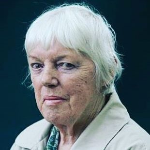 A woman with short white hair looks intently at the camera