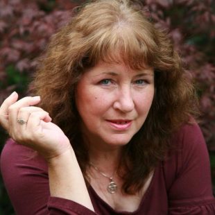 A woman with reddish brown hair looks up at the camera and has her right hand up near her face