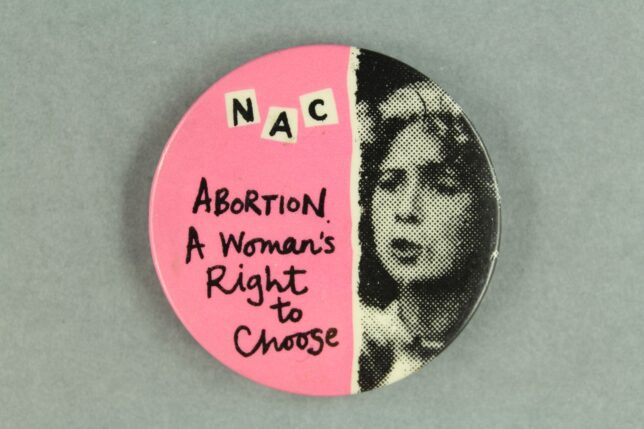 A pink badge with a black and white image of a woman's face to the right. On the left is written, "Abortion, A woman's right to choose".