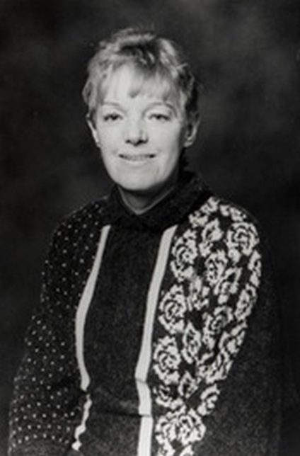 A black and white image of Agnes Owens. She is smiling at the camera and it appears the image was taken in a studio.