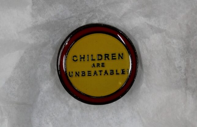 An enamel badge with a yellow centre and a red band around its circumference. In the centre the words, "Children are unbeatable" are written in block capitals.