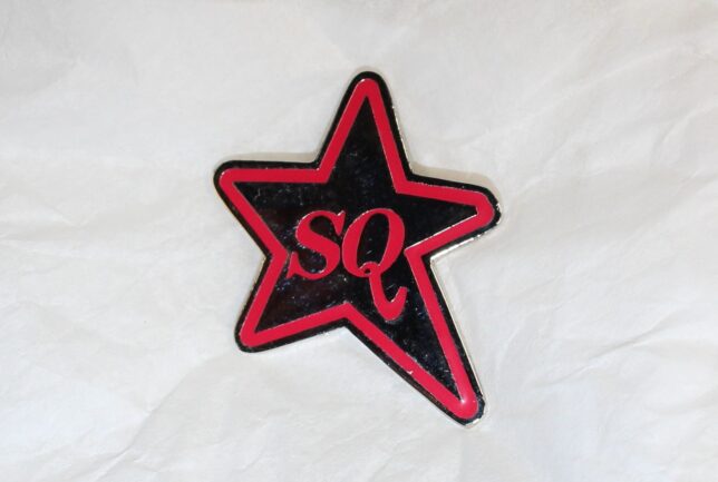 A black and red badge in the shape of a star. It has the letters S and Q at its centre.