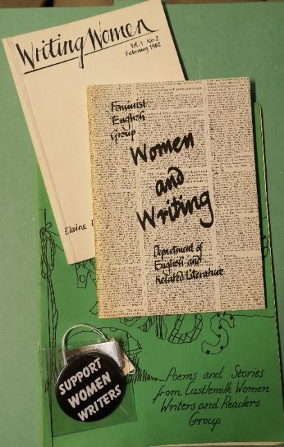 Two paper items and a badge arranged together. The badge says, "Support Women Writers"