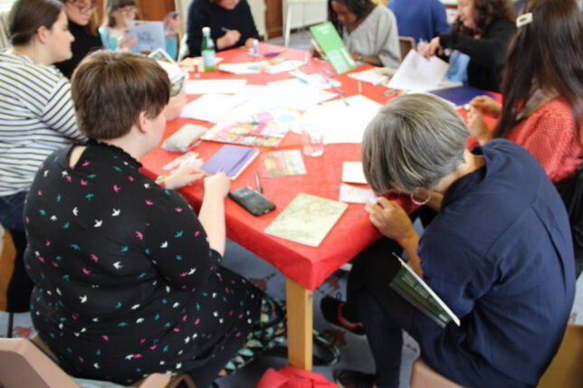 Women gathered around a table, their heads bent over paper; they're all busy working at their creative task.