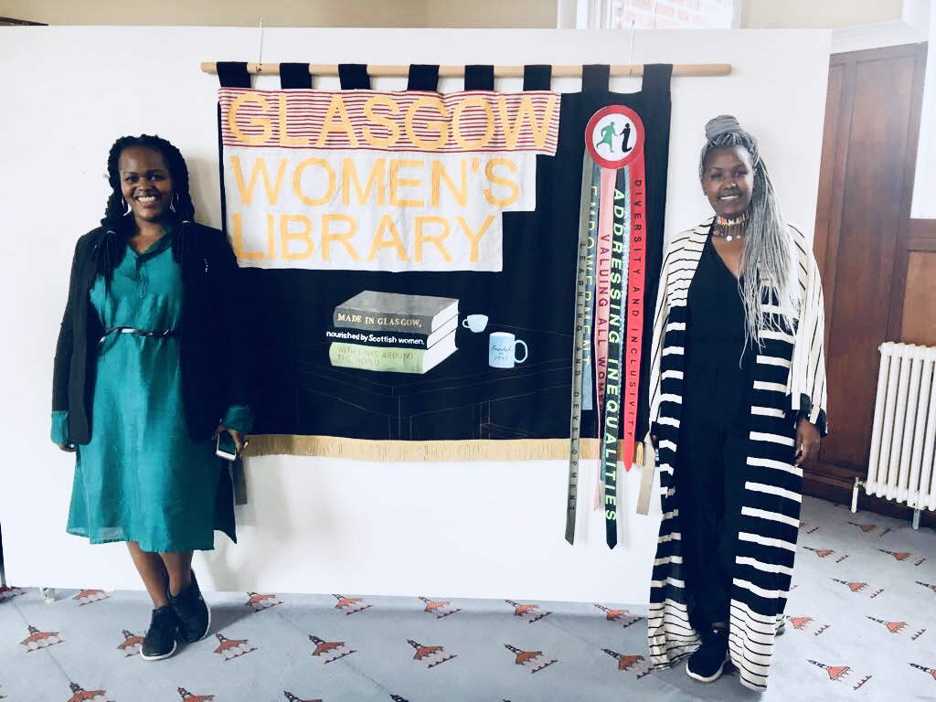 Two women standing in front of a banner that says 'Glasgow Women's Library'