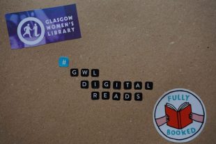 Image of a decorated piece of recycled cardboard. Stickers in the centre of the cardboard spell out the hashtag GWL Digital Reads. In the top left-hand cornern is a cut out logo of the Glasgow Women's Library. In the bottom right corner is a round sticker with an illustration of two hands holding an open book with a red cover. The sticker reads fully booked in turquoise.