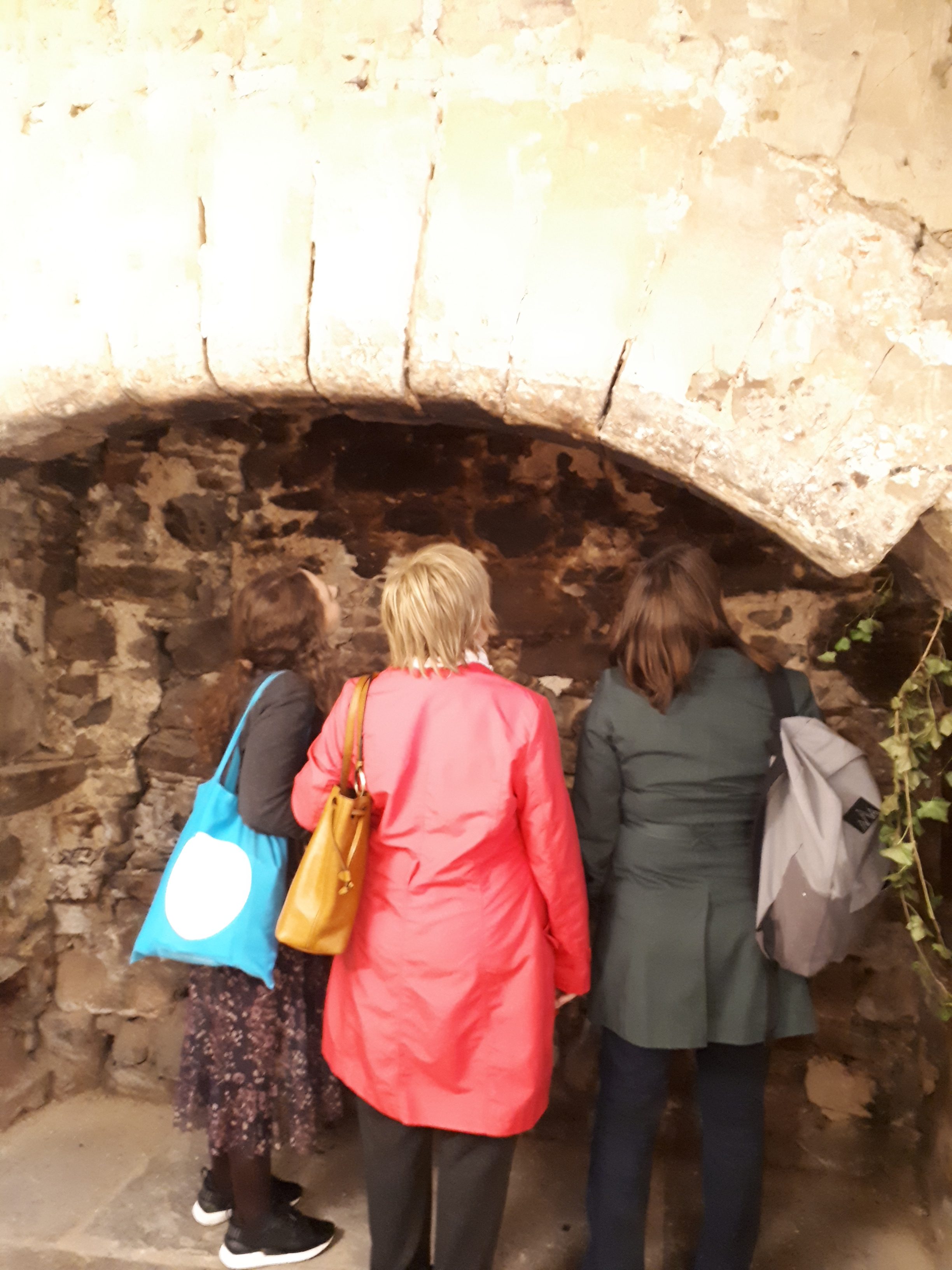 Three women look at a brick wall. We just see their backs.