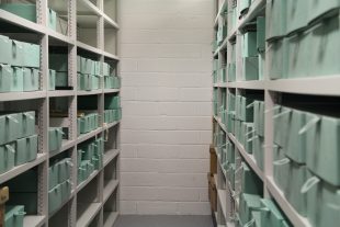 Photograph of the inside of one of GWL's archive stores showing pale green archive boxes stacked on long shelves.