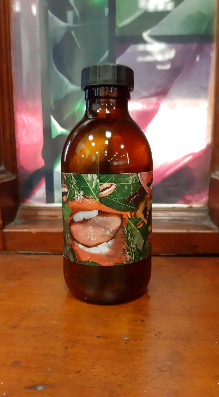 Brown bottle with black lid, with Linder's design on the label. The design is of open mouths with pink lips, with greenery and leaves surrounding it.