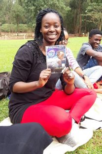 A young woman smiling to the camera and holing up a book.