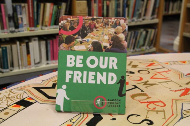 A display of GWL Friends leaflets with the title 'Be Our Friend' stands on a colourful table with bookshelves behind.