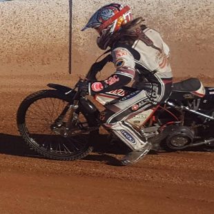 young female in full leathers on speedway bike riding on dirt track  