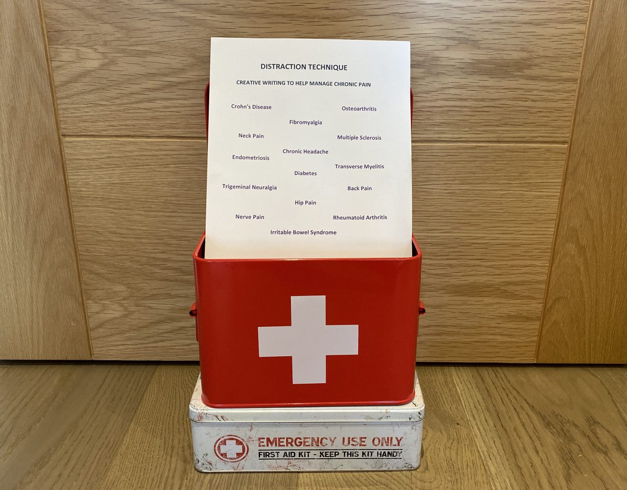 A red first aid box with a piece of paper standing in it. The paper is titled ‘Distraction Technique’ and has words like ‘Hip Pain,’ ‘Multiple Sclerosis,’ and ‘Fibromyalgia’ on it.