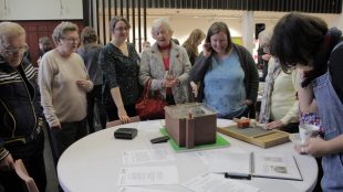 At the Community Curators' pop-up event, women around a table look at some of the selected objects, including a old-fashioned washboard