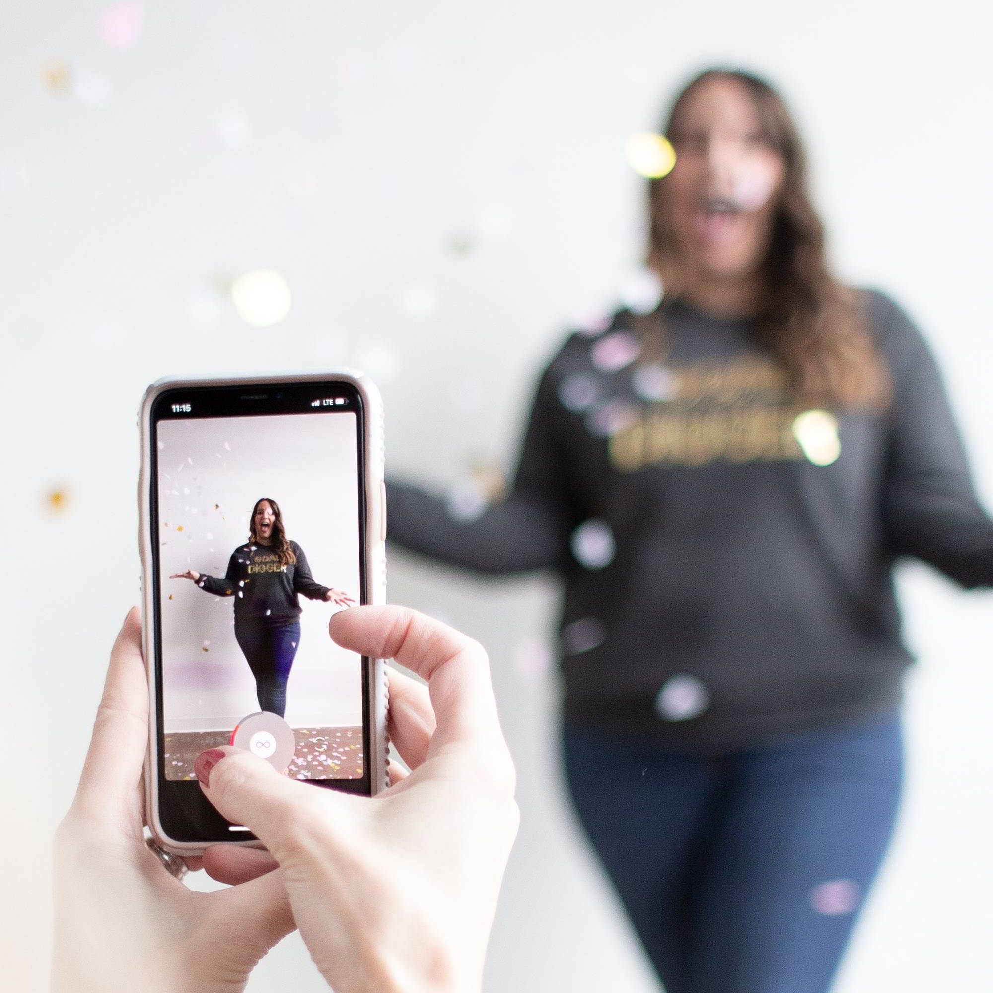 A phone filming a woman who is standing against a white wall