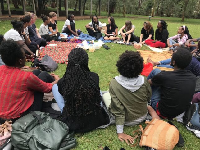 Image taken by Adele on her Clore Leadership Fellowship showing a group of women from Book Bunk and GWL sitting around in a circle on the grass listening to one woman, Wanjiru Koinange, as she talks.