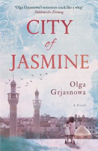 Cover of the City of Jasmine book. The background is a washed out light blue and pink colour with a water-coloured effect. In the bottom left corner of the book two children stand on a rooftop, the taller of the two has his arm around the smaller one. Their heads are pressed together. They are looking out at the city before them.