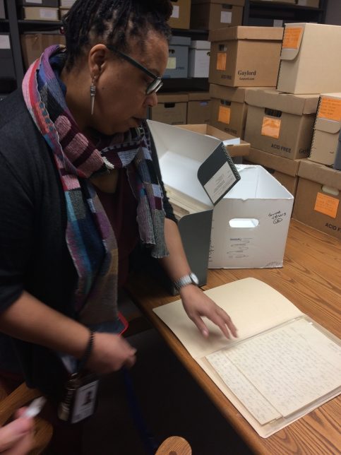 Image taken by Adele on her Clore Leadership Fellowship shows a woman, Lynora Williams looking at a handwritten letter within an archive, surrounded by archival boxes.