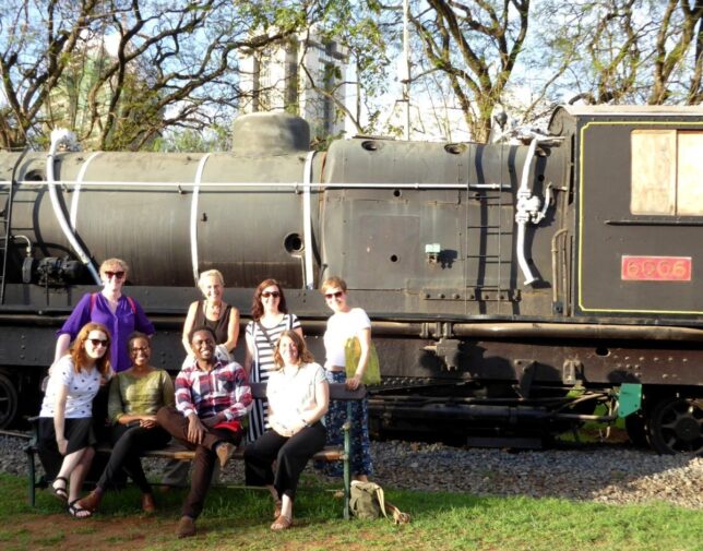 Seven women and one man grouped in front of a large locomotive engine at Nairobi Railway Museum