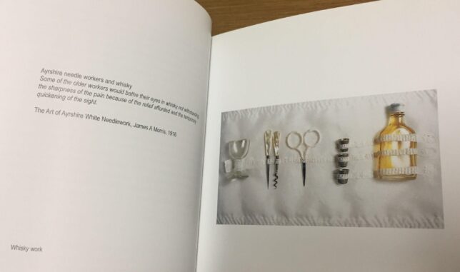 Exhibition catalogue open at a page titled 'Whisky work' featuring an image of needlework tools alongside a miniature whisky bottle