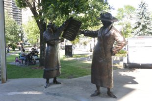 Bronze statue of two women in early 20th century dress holding up a newspaper which reads: "Women are Persons"