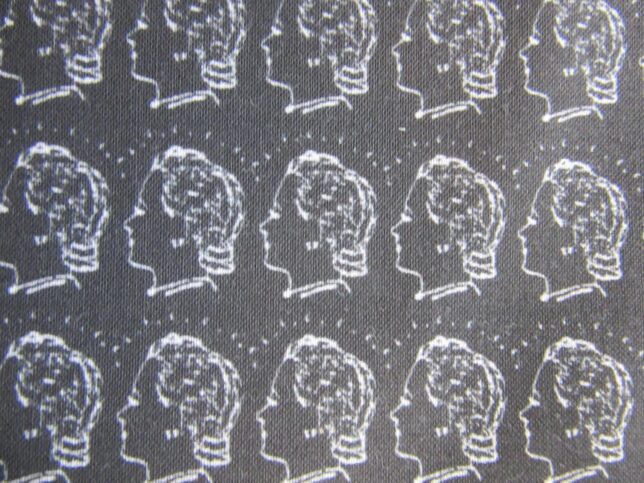 Patterned fabric design for our GWL facemasks, in white on black with the 'Women in Profile' logo from GWL's precursor, a woman's head with short lines radiating outwards.