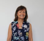 Dorothy stands against a white background. Dorothy wears a floral sleeveless blouse. Dorothy is smiling