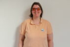 Doreen stands against a white wall. Doreen wears a peach polo shirt. Her hair is in a bob style and she wears glasses with orange tinted lenses. 