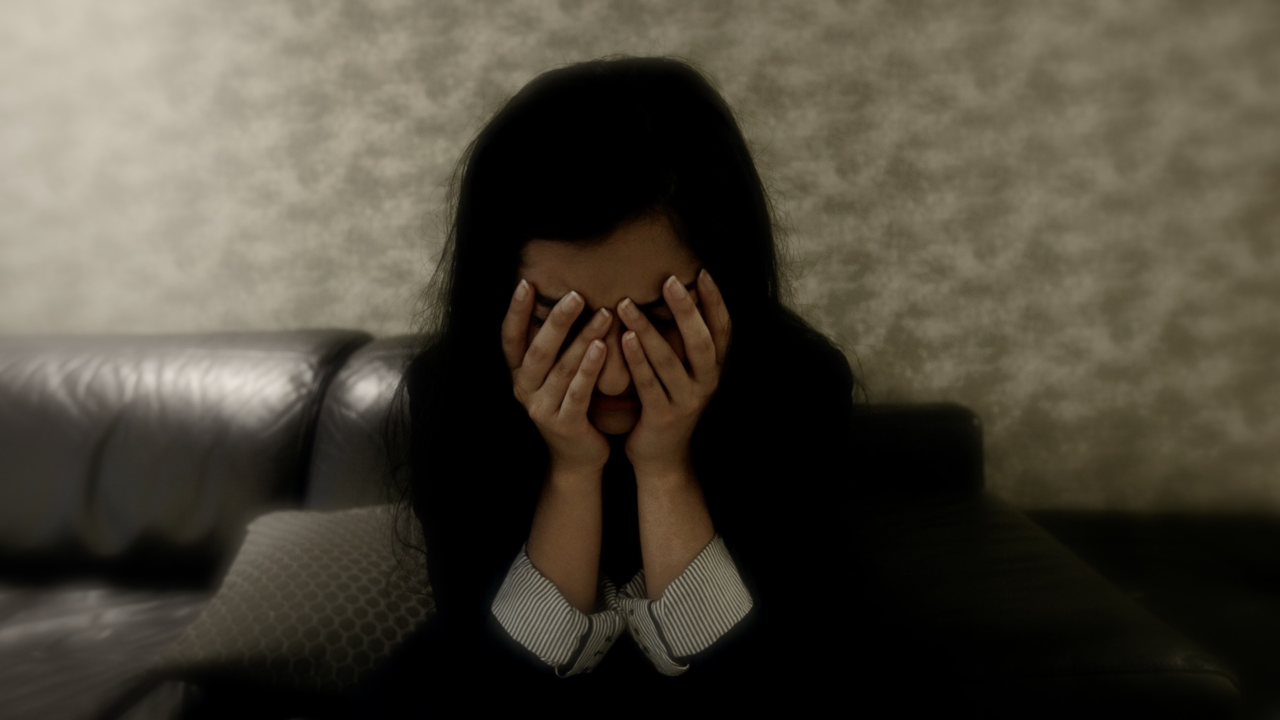 A woman sits with her hands over her face.