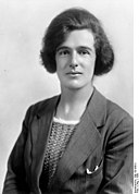 Black and white waist up photograph of Jessie Stephen. A white woman with a dark hair. She is looking into the camera and has a confident and gentle look on her face. 