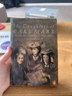 Hand holding a copy of 'The Daughters of Karl Marx' which depicts the three sisters photographed together on the cover