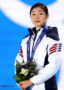 Yuna Kim smiling, wearing her competition outfit and a medal, holding a bouquet.