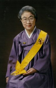 Lee Tai-young sitting down, wearing a purple Hanbok (traditional Korean dress) with a gold sash.