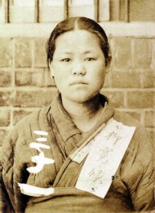 Photo of Yu Gwan-sun. Her hair is up and she is wearing a worn-out hanbok (traditional Korean dress). A piece of paper is attached to it. She is looking straight into the camera.