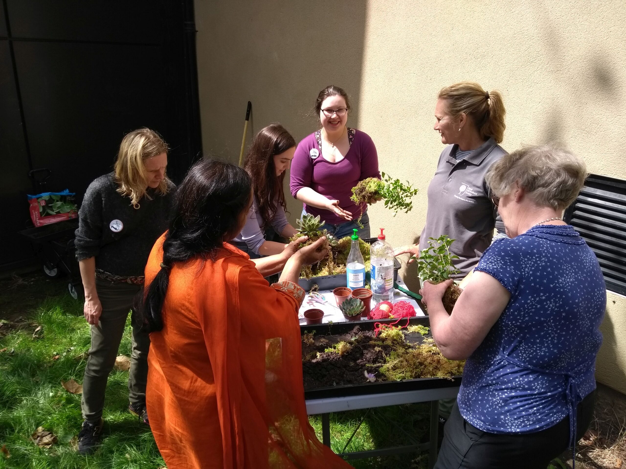 The GWL Green Cluster gathered round a table full of plants, preparing them to be planted.